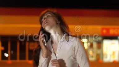 年轻女子晚上在<strong>停车</strong>场的智能手机上用灯笼说话。 很漂亮的女孩在打<strong>电话</strong>